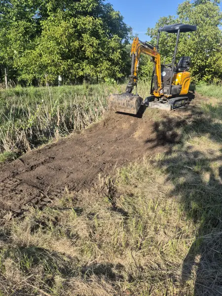 A minikotró megkezdi a gaz és a gyökérzet leszedését.